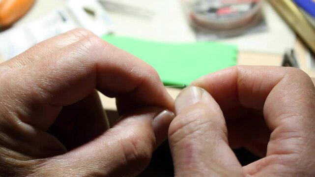 A person uses sleight of hand to securely tie a fishing line to a fishing hook, making a fisherman's knot.