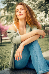 Obraz premium Young woman with curly red hair enjoying a sunny spring day in the park wearing casual jeans and stylish outfit