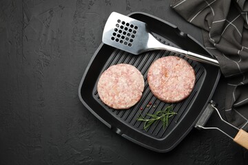 Fresh raw patties for burger and spices in frying pan on black table, top view. Space for text