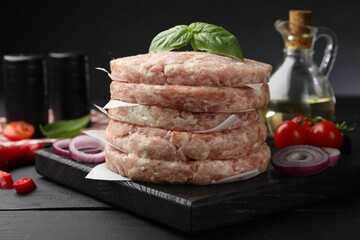 Fresh raw patties for burger, spices and tomatoes on black wooden table, closeup