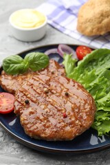 Delicious hamburger patties, tomato, lettuce and spices on grey table, closeup