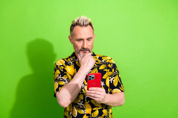 Mature man with trendy summer shirt viewing smartphone against a vibrant green backdrop
