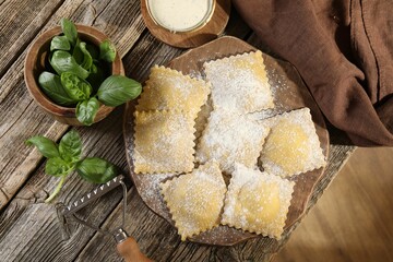 Uncooked ravioli and basil on wooden table, top view