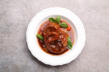Traditional ossobuco dish with beef steak and sauce on grey table, top view.