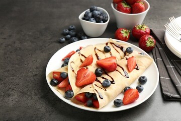 Tasty crepes with strawberries, blueberries and chocolate sauce on gray textured table, closeup