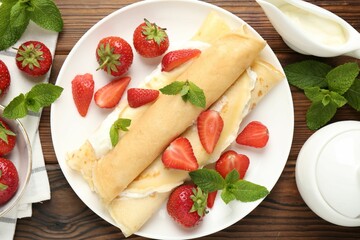 Tasty crepes with cream, strawberries and mint on wooden table, flat lay