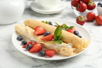 Tasty crepes with cream, berries and mint on white marble table, closeup