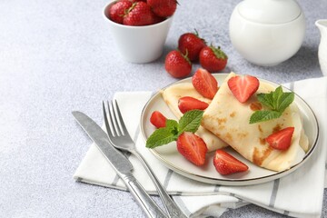 Tasty crepes with cream, strawberries and mint served on light gray textured table, closeup
