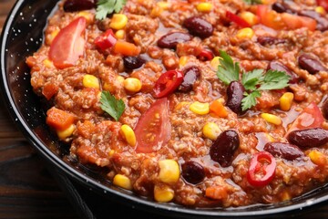 Tasty chili con carne in baking dish on wooden table, closeup