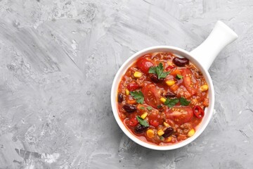 Tasty chili con carne in bowl on grey textured table, top view. Space for text