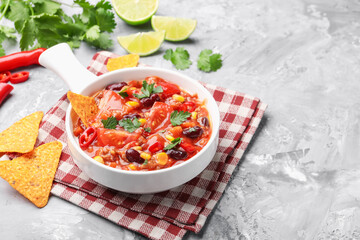 Tasty chili con carne in bowl and nachos on grey textured table, closeup. Space for text
