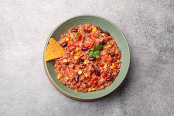 Tasty chili con carne in bowl and nachos on grey table, top view
