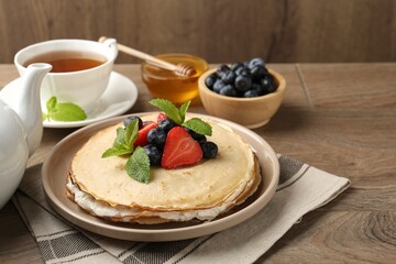 Delicious crepes with berries, cream, mint, honey and tea on wooden table, closeup