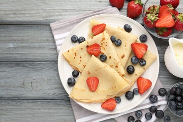 Delicious crepes with berries and cream on grey wooden table, flat lay. Space for text