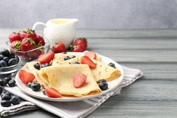 Delicious crepes with berries and cream on grey wooden table, closeup. Space for text