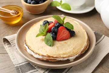 Delicious crepes with berries, cream, mint and honey on wooden table, closeup