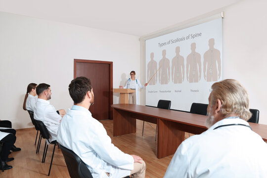 Healthcare professional giving lecture about scoliosis in conference room using video projector. Illustrations on projection screen