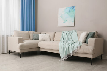 Comfortable sofa near window with light blue curtains in room. Interior design