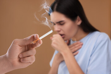 Passive smoking. Woman coughing because of man smoking nearby on pale brown background. Selective focus