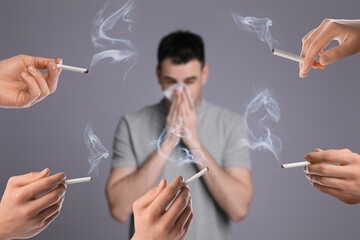 Passive smoking. Man covering his nose with tissue because of people smoking nearby on grey...