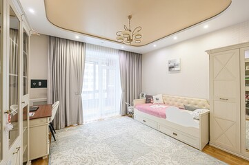 bright children's room features a daybed, desk, wardrobe, and a large window with curtains. The...