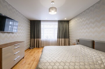 modern bedroom features a bed, dresser, and a wall-mounted TV. The room is decorated in neutral...