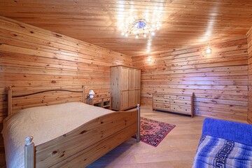 Cozy bedroom with wooden walls, ceiling, and furniture.  A bed is present, with a rug and dresser...
