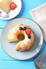 Tasty bundt cake with powdered sugar and berries on light blue wooden table, flat lay