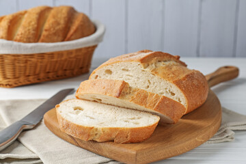 Cut bread loaf and knife on white wooden table, closeup