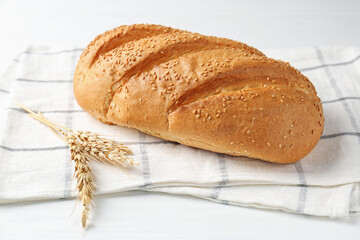 Fresh bread loaf and spikelets on white wooden table, closeup