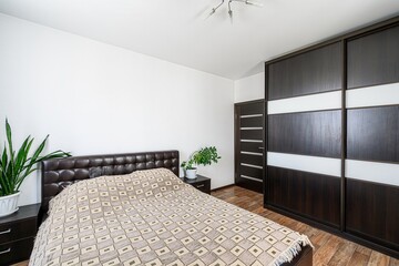 bedroom features a brown leather bed, a sliding door wardrobe, white walls, and wooden flooring
