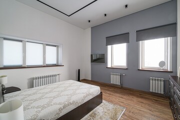 modern bedroom with a queen size bed, white and grey walls, and three windows. The room features...