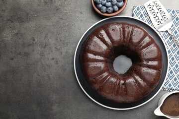 Tasty chocolate bundt cake, blueberries and server on grey table, flat lay. Space for text