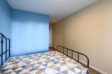 bedroom with blue and beige walls, a metal bed frame, and a geometric patterned duvet. A doorway is...