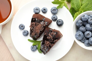 Pieces of delicious bundt cake with blueberries, mint and chocolate shavings on wooden table, flat lay