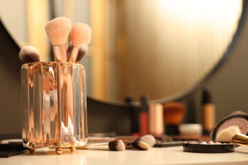 Different makeup products and brushes on dressing table indoors, closeup
