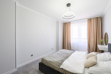 Bright bedroom features a bed with neutral bedding, a window with beige curtains, and minimalist decor