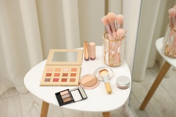 Different makeup products and brushes on white table near mirror indoors