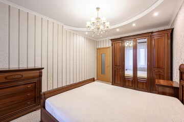Cozy bedroom with a bed, wooden furniture, striped wallpaper, and a chandelier