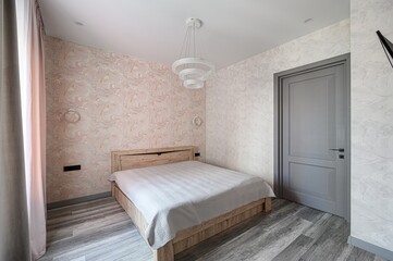 Cozy bedroom with a wooden bed, patterned walls, and a modern chandelier. Gray door and striped bedding