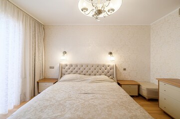 serene bedroom featuring a large bed with a tufted headboard, soft lighting, and neutral tones...