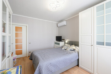 cozy bedroom with a gray bed, white cabinets, and a modern ceiling light. The room is bright and airy