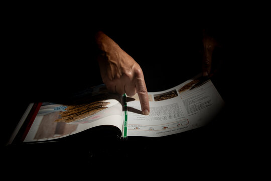 Primer plano de una mano humana se&ntilde;alando un libro de recetas en fondo oscuro con iluminaci&oacute;n puntual que resalta el gesto de lectura