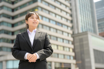 都会のビルを背に立ちスーツに身を包む若手フレッシャーズの女性