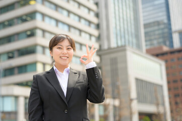 晴天のビル街で元気よく手を振るスーツ姿のフレッシャーズ