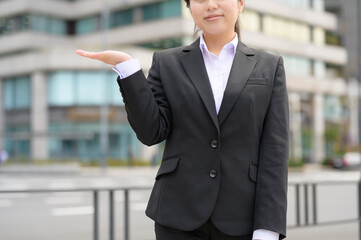 左手を横に出して案内するような仕草を見せるスーツ姿の新入社員
