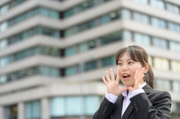 笑顔で顔の横に手を添えて元気に呼びかけるスーツ姿の新入社員