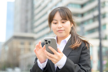 スマートフォンを両手で持ち楽しそうに見つめるスーツ姿の女性