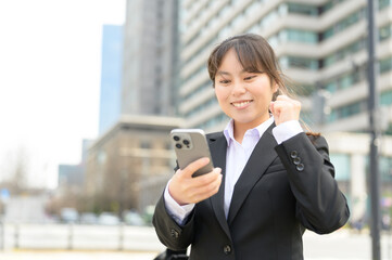Fototapeta premium スマートフォンを見ながらガッツポーズをする喜びに満ちたフレッシャーズの女性