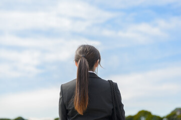 スーツ姿の若い女性が青空の下で背中を向けて立っている後ろ姿
